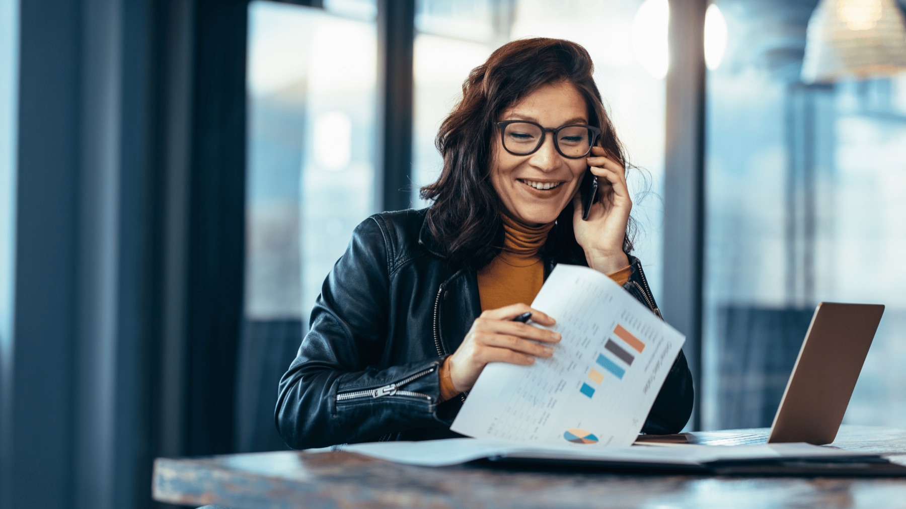 A small business owner on the phone, reviewing a printed security readiness summary with charts at her desk