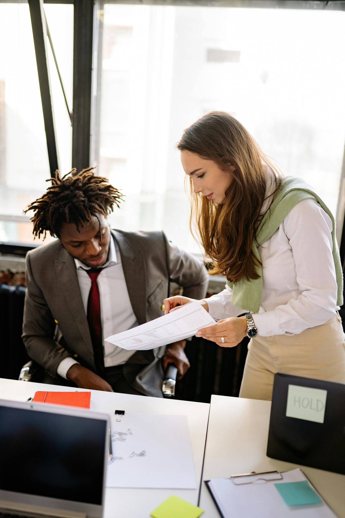 A small business owner handing a printed summary to a broker across a desk